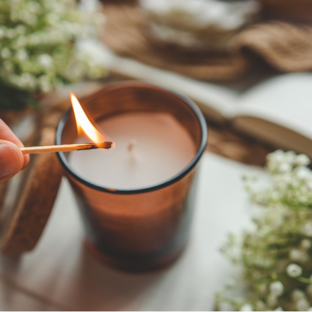 Hand zündet eine Duftkerze an, daneben ein Notizbuch für persönliche Hygge-Rituale